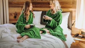 Two people in green robes sitting on a bed in a wooden cabin room. - Wellnesshotel Hofbräuhaus (Bodenmais)