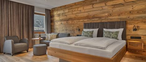 A modern bedroom with a wooden headboard, a large bed, a grey sofa, and a small side table with a wine bottle.