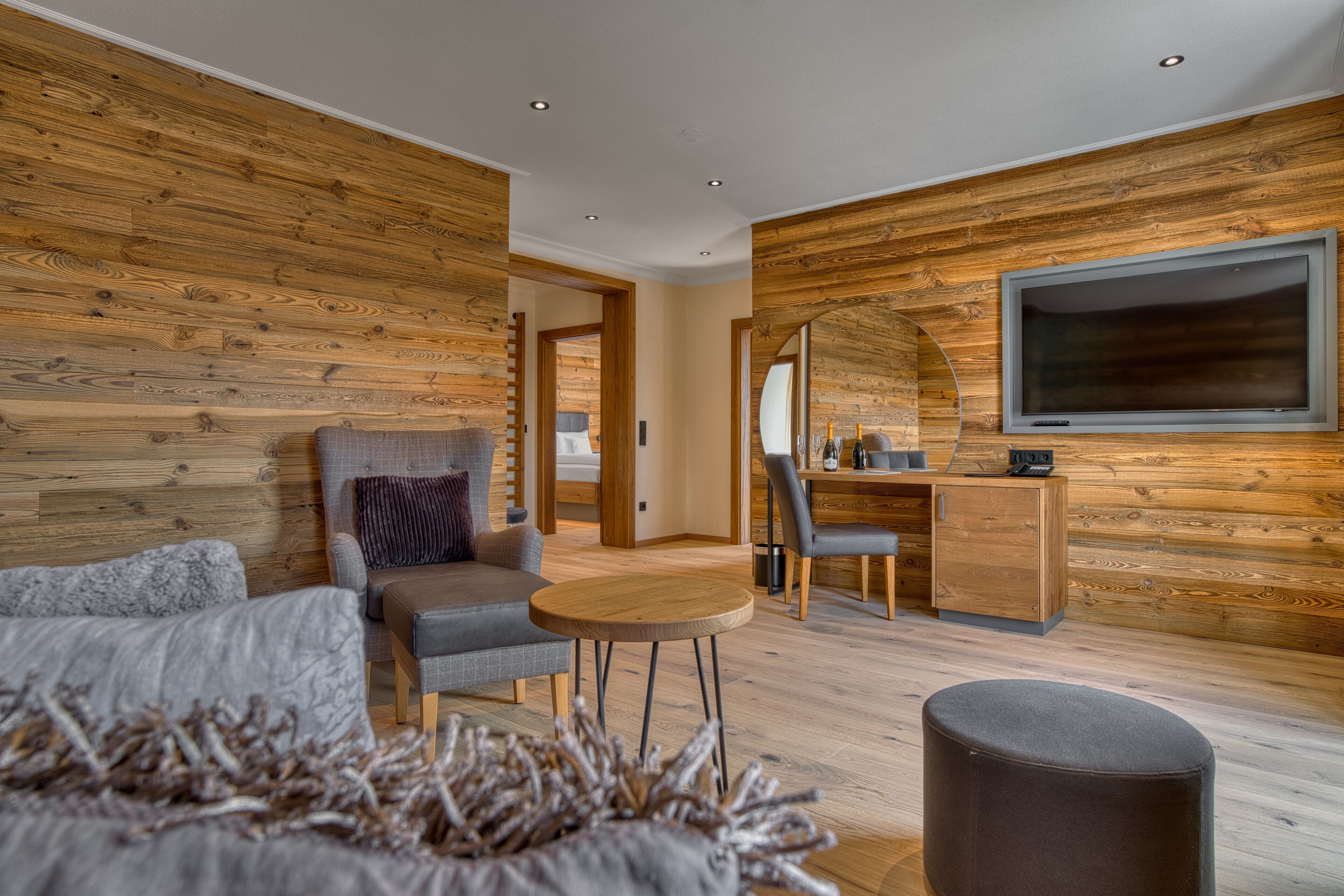 Une chambre moderne avec des murs recouverts de panneaux de bois, un lit, un coin salon avec une table et un téléviseur fixé au mur.