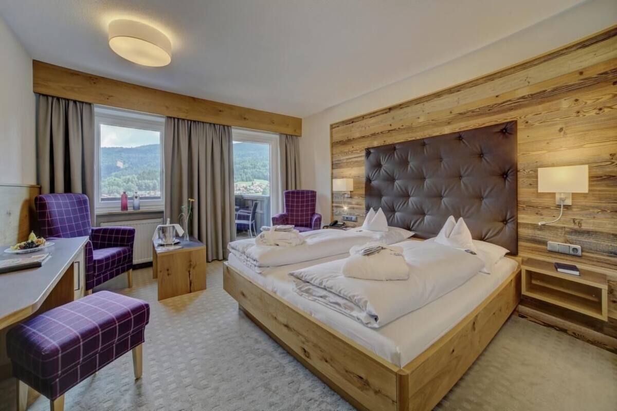 Une chambre d’hôtel avec un grand lit, deux fauteuils, un bureau et une vue sur l’extérieur.