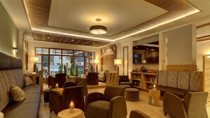 A cozy lounge area with sofas, armchairs, and a fireplace. There are large windows providing natural light and a view of the outside. - Wellnesshotel Hofbräuhaus (Bodenmais)