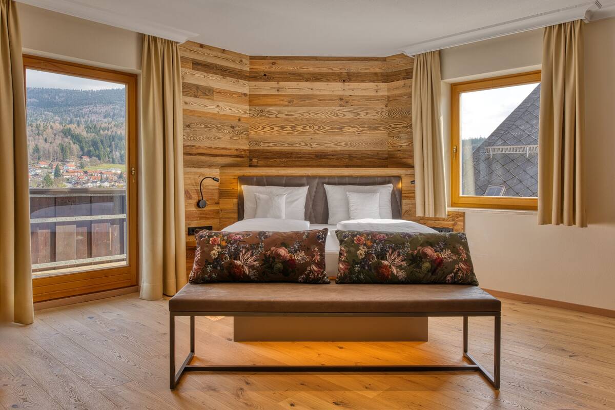 Une chambre avec un mur recouvert de lambris en bois, un grand lit agrémenté d’oreillers à motifs floraux et un banc.