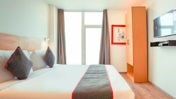 Een hotelkamer met een groot bed, een houten garderobe, een televisie en een raam met gordijnen.