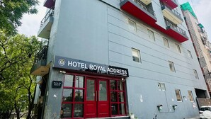 Een meerlaags hotel met een rode en grijze gevel, een opvallende ingang met rode deuren en een trap die naar de ingang leidt.