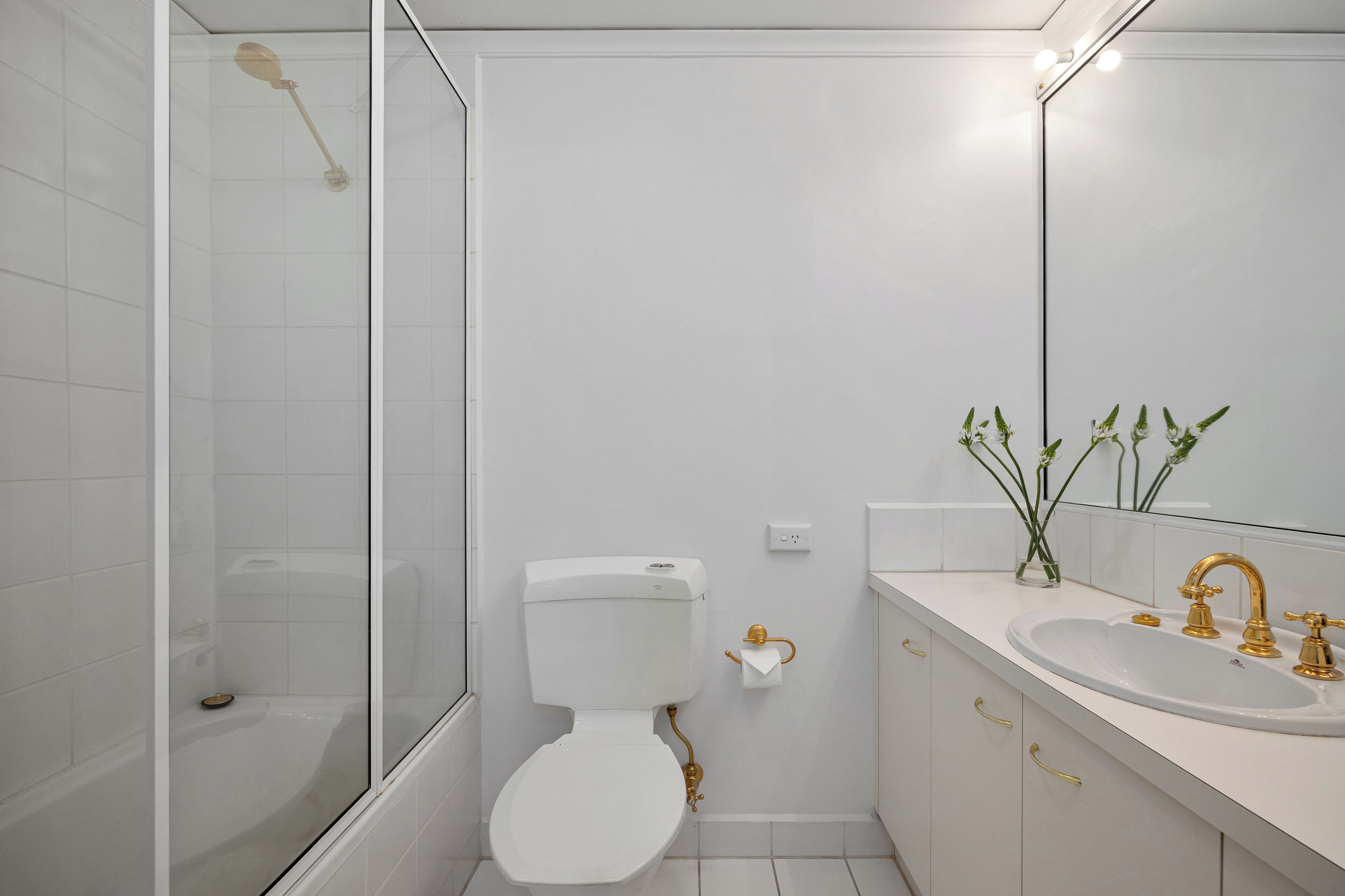 A modern bathroom with a glass-enclosed shower, a white toilet, and a sink with gold fixtures.