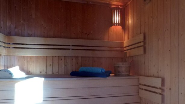 Un sauna aux murs en bois, avec un banc, une serviette bleue et un seau.