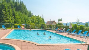 Une piscine rectangulaire, bordée d’une terrasse carrelée, entourée de chaises longues bleues et d’une petite piscine circulaire.