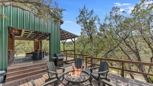 Eine Terrasse mit Feuerstelle, Sitzgelegenheiten im Freien und einem überdachten Grillbereich.