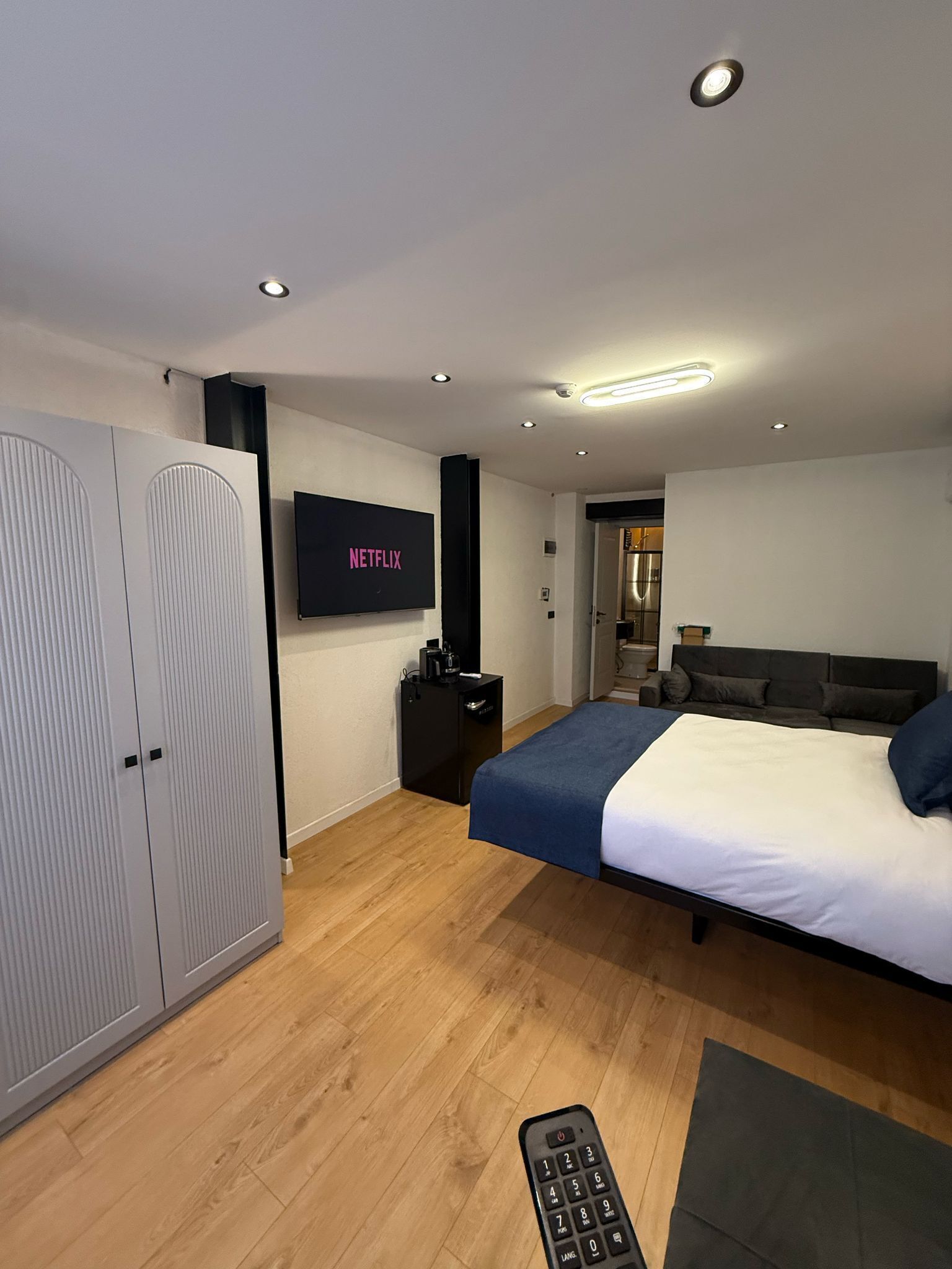 A modern bedroom with a bed, wardrobe, TV, and a remote control on the floor.