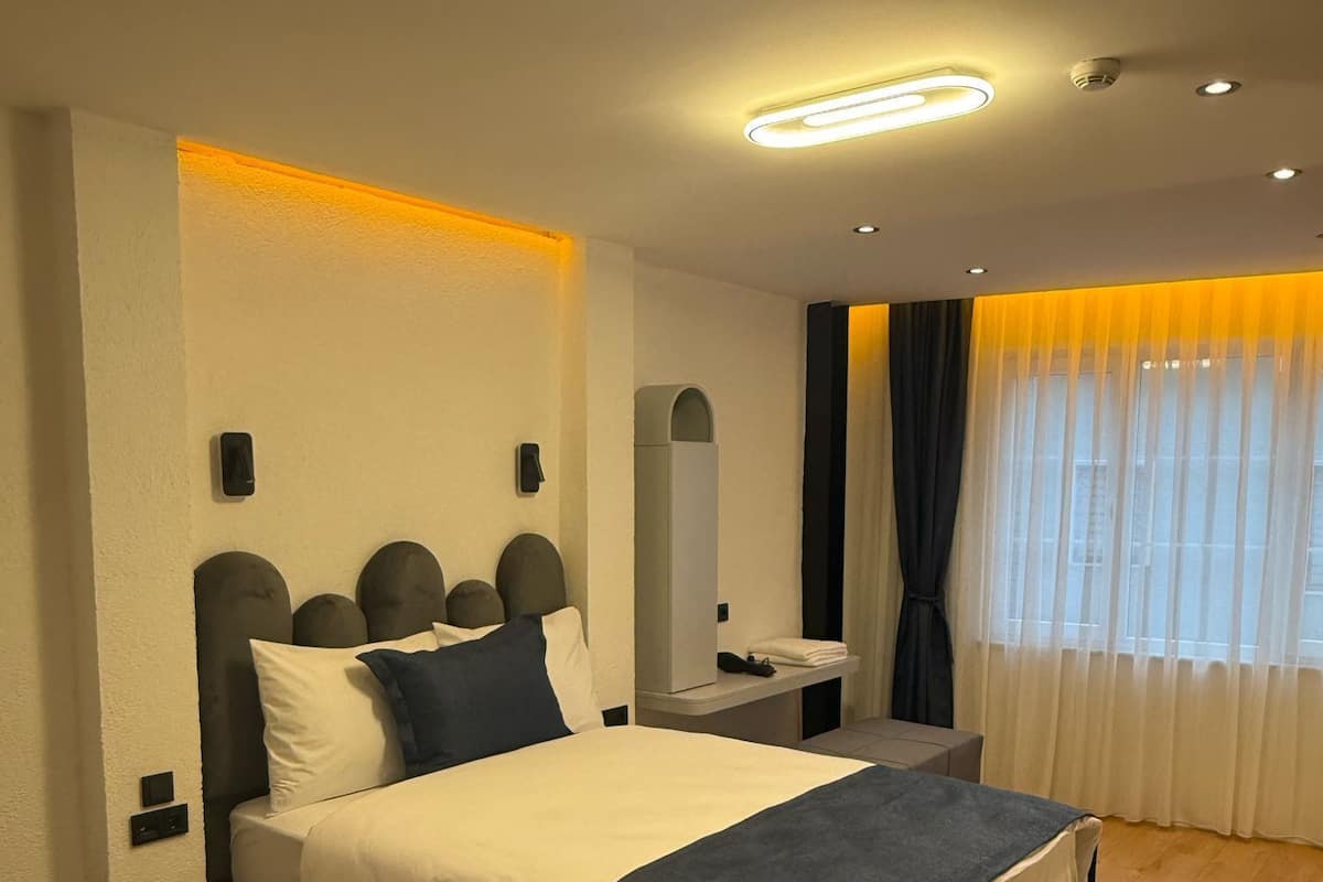 A modern bedroom with a bed, bedside tables, a nightstand, a mirror, and a window with curtains.