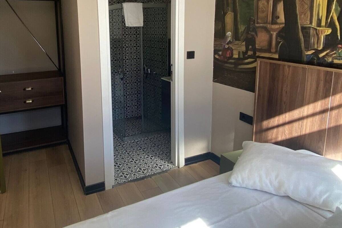 A bedroom with a bed, a door leading to a bathroom, a painting on the wall, and a ceiling light.