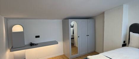A modern bedroom with a bed, a vanity with a mirror, a wardrobe, and a small desk area.