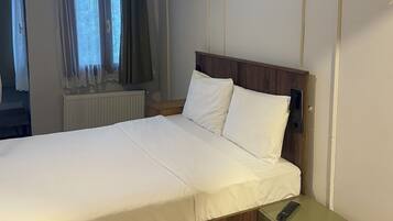 Un letto rifatto con cura, una testiera in legno, un comodino con un telecomando e un tavolino da notte verde.