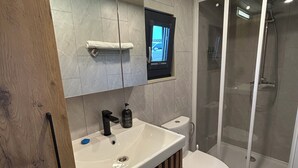 A modern bathroom with a wooden vanity, a white sink, a toilet, and a glass shower enclosure. - The Highland Cow Bothy (Longridge)