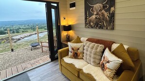 A cozy living room with a sofa, cushions, and a painting of a cow. - The Highland Cow Bothy (Longridge)