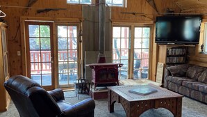 Interior acogedor de una cabaña con un techo grande de madera, una chimenea, un sillón de cuero, una mesa de centro de madera y un televisor.
