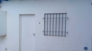 Pared exterior blanca con una puerta y un ventanal con barrotes.