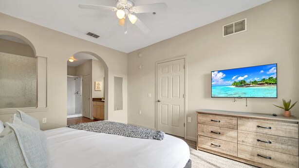 Un dormitorio con cama, televisor, ventilador de techo, cómoda y una puerta.
