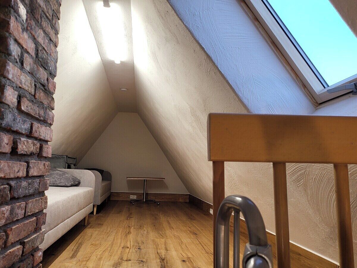 A small, sloped ceiling room with a sofa, a small table, and a brick wall.