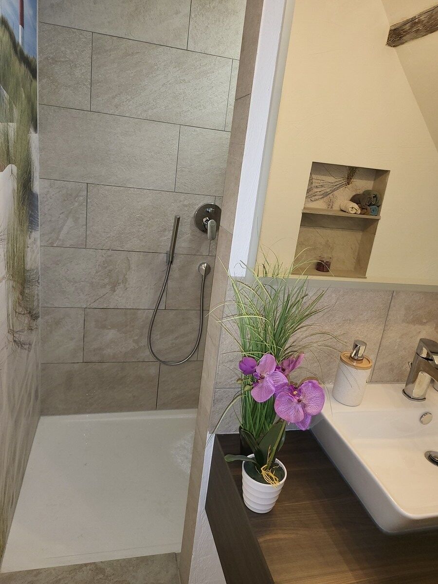 Ein Badezimmer mit Dusche, Waschbecken und einem kleinen Ablagebereich für Pflegeprodukte.
