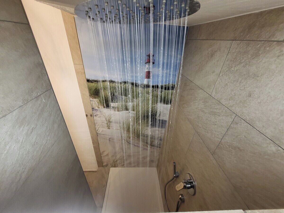 Ein modernes Badezimmer mit Duschkabine, freistehender Wasserhahn und Blick auf eine sandige Landschaft.