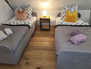 A room with two beds, a nightstand with a lamp, and a wooden floor.