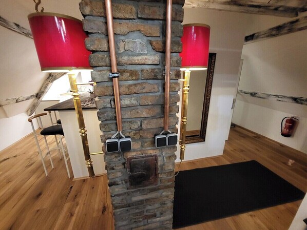 A room with a stone wall, wooden floor, a black mat, a chair, a table, and a red lamp.