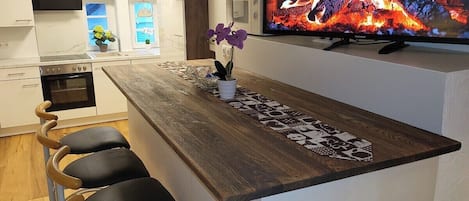 A modern kitchen with a wooden bar counter, a television displaying a fire, and a bar stool seating arrangement.
