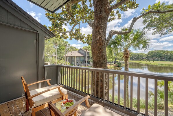 A wooden deck with a bench and table, overlooking a body of water and a distant building.