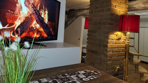 A modern living room with a flat-screen TV displaying a fireplace, a brick wall, and a staircase with a red accent wall.