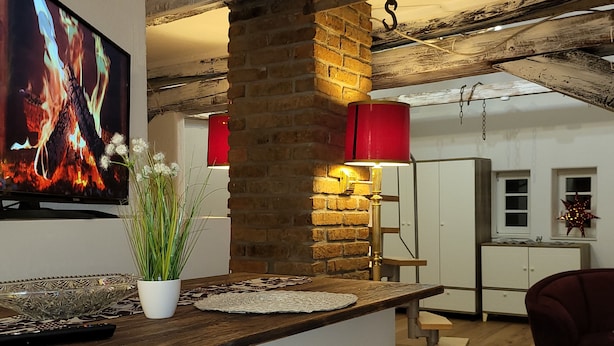 A modern kitchen with a brick wall, a wooden countertop, and a red hanging light fixture.