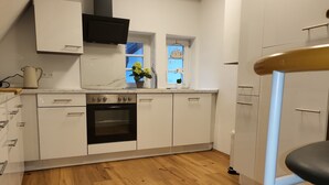 A modern kitchen with white cabinetry, a built-in oven, and a window with a view of trees.