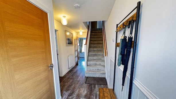A hallway with a wooden door, a staircase, and a coat rack with hanging items.