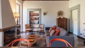 Een woonkamer met een open haard, een bank, twee fauteuils, een salontafel en een boekenkast.