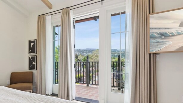 A bedroom with a bed, a chair, and a balcony with a view of the city. - Casa Riviera 26 - Boutique Suites (Santa Barbara)