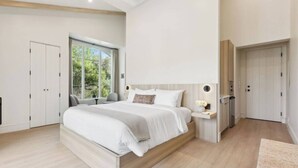 A modern bedroom with a large bed, built-in nightstand, and a window with a view of greenery. - Casa Riviera 26 - Boutique Suites (Santa Barbara)