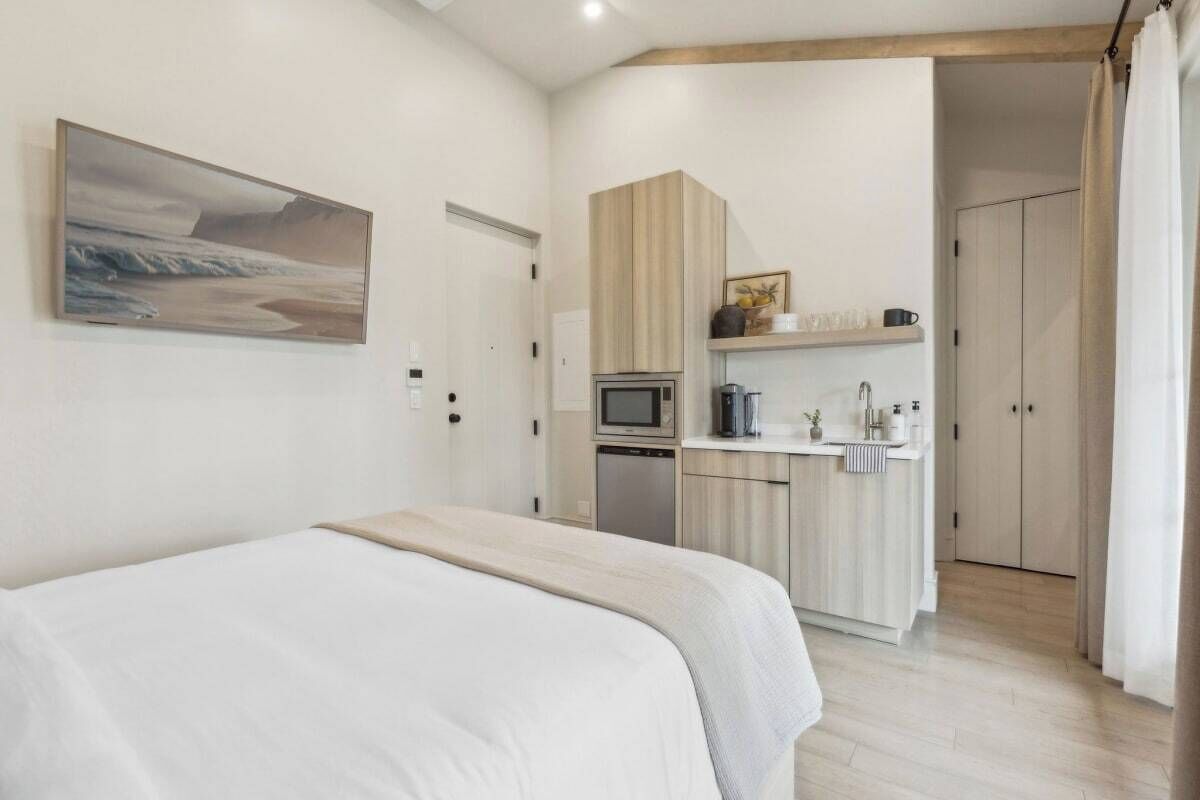 Quarto com cama, cozinha compacta com micro-ondas e porta que dá para outro cômodo.