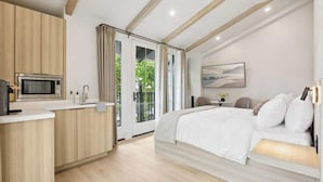 A modern hotel room with a kitchenette, a large bed, and a view of greenery outside. - Casa Riviera 28 - Boutique Suites (Santa Barbara)