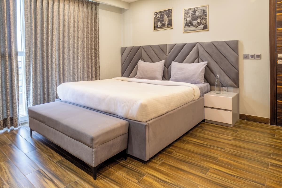 A modern bedroom with a large bed, a bench, a nightstand, and a wooden floor.