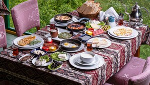A table set outdoors with various dishes, a teapot, and a glass of tea. - Chukhur Gabala Museum Hotel (Gabala)