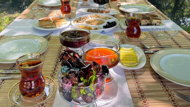 A table set outdoors with various dishes and drinks, surrounded by trees and a body of water. - Chukhur Gabala Museum Hotel (Gabala)