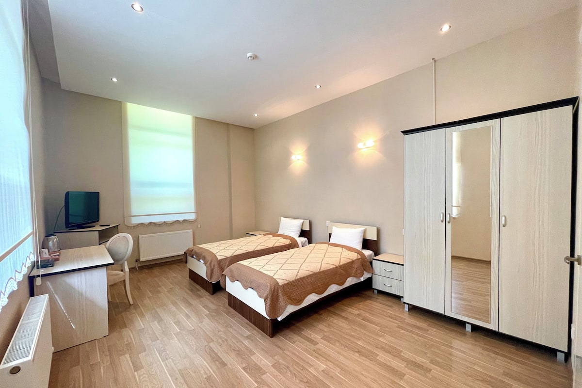 A bedroom with two beds, a desk, a chair, and a wardrobe.