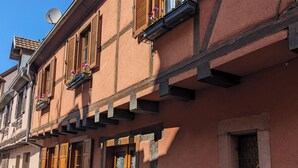Um edifício europeu tradicional com fachada de pedra, persianas de madeira e caixas de flores nas janelas.