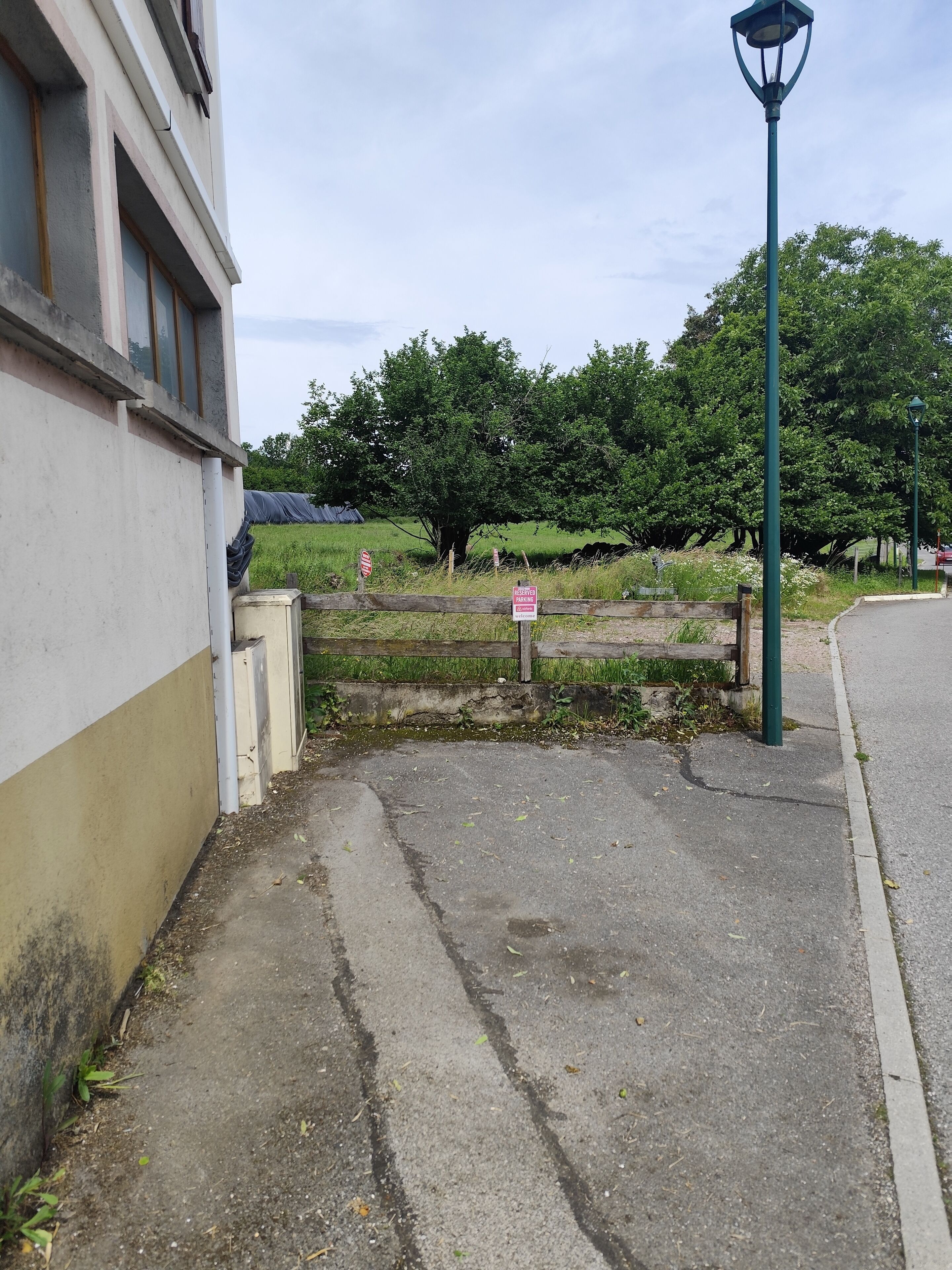 A paved pathway leading to a building with a 'Reserved Parking' sign, a lamp post, and a grassy area with trees in the background.