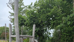 Un’area giochi con scivolo e strutture per arrampicarsi, circondata da alberi e ghiaia.