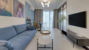 A modern living room with a blue sofa, a coffee table, a TV, and artwork on the walls. - Żurawie IKONY 1 by Grand Apartments (Gdansk)