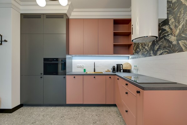 Una cocina moderna con armarios grises y rosados, un refrigerador de acero inoxidable y una encimera negra.