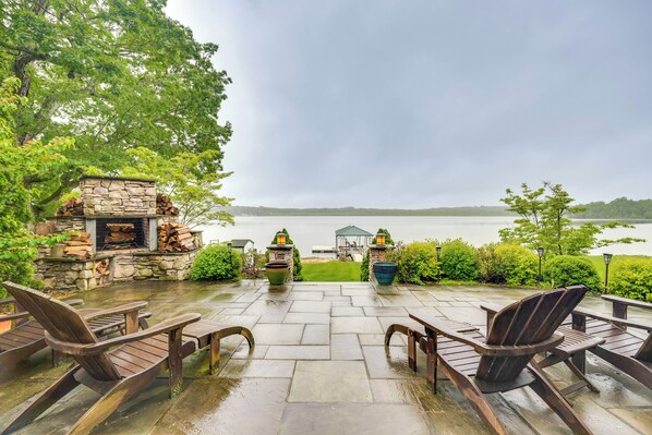 A patio with stone flooring, wooden chairs, and a stone fireplace. - Luxe Family Home on Orange Lake w/ Private Dock! (Newburgh)