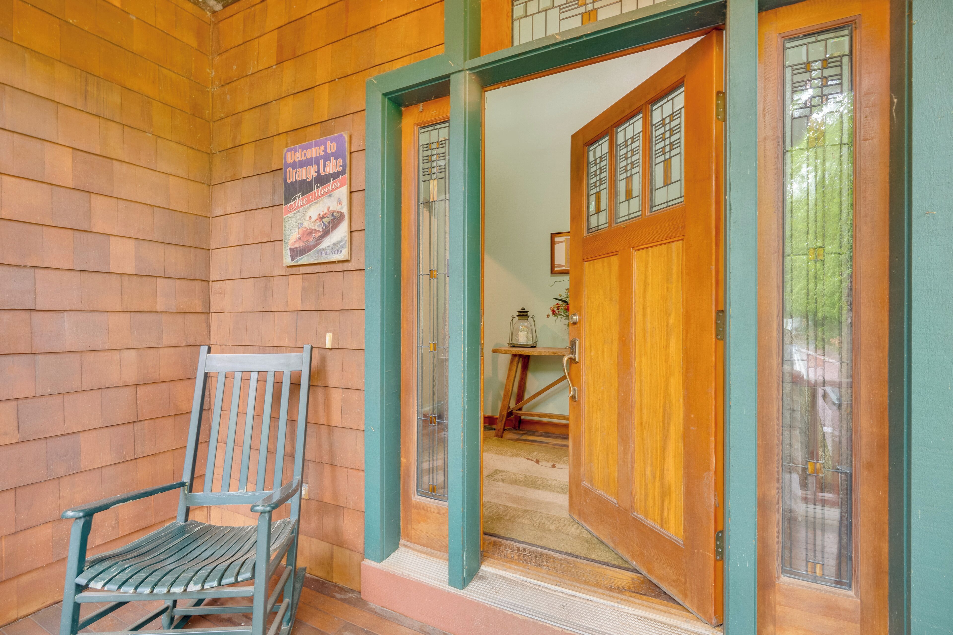 A wooden exterior with a wooden chair, a door with glass panels, and a welcome sign.