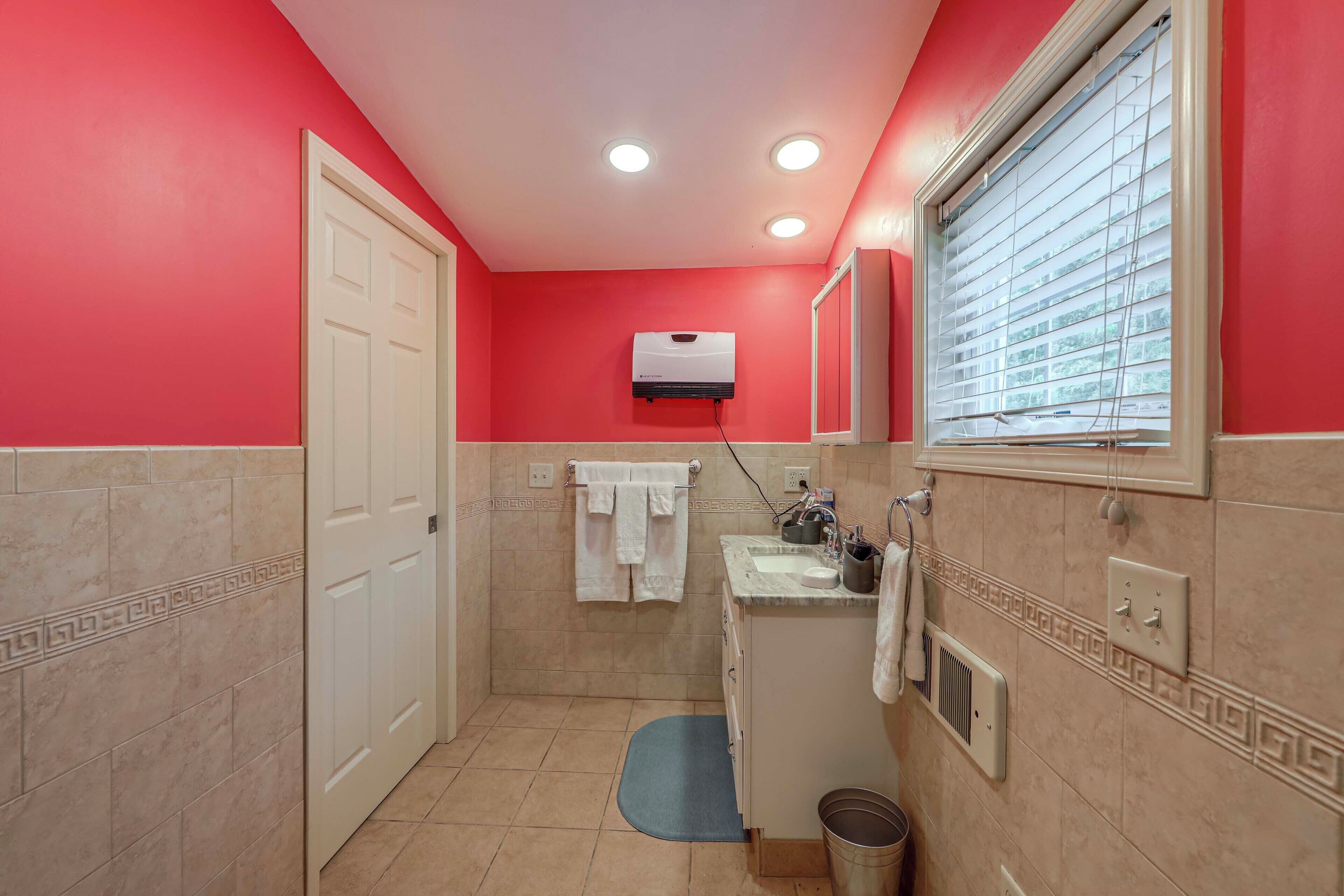 A bathroom with red walls, a white door, a sink with a mirror, and a window with blinds.